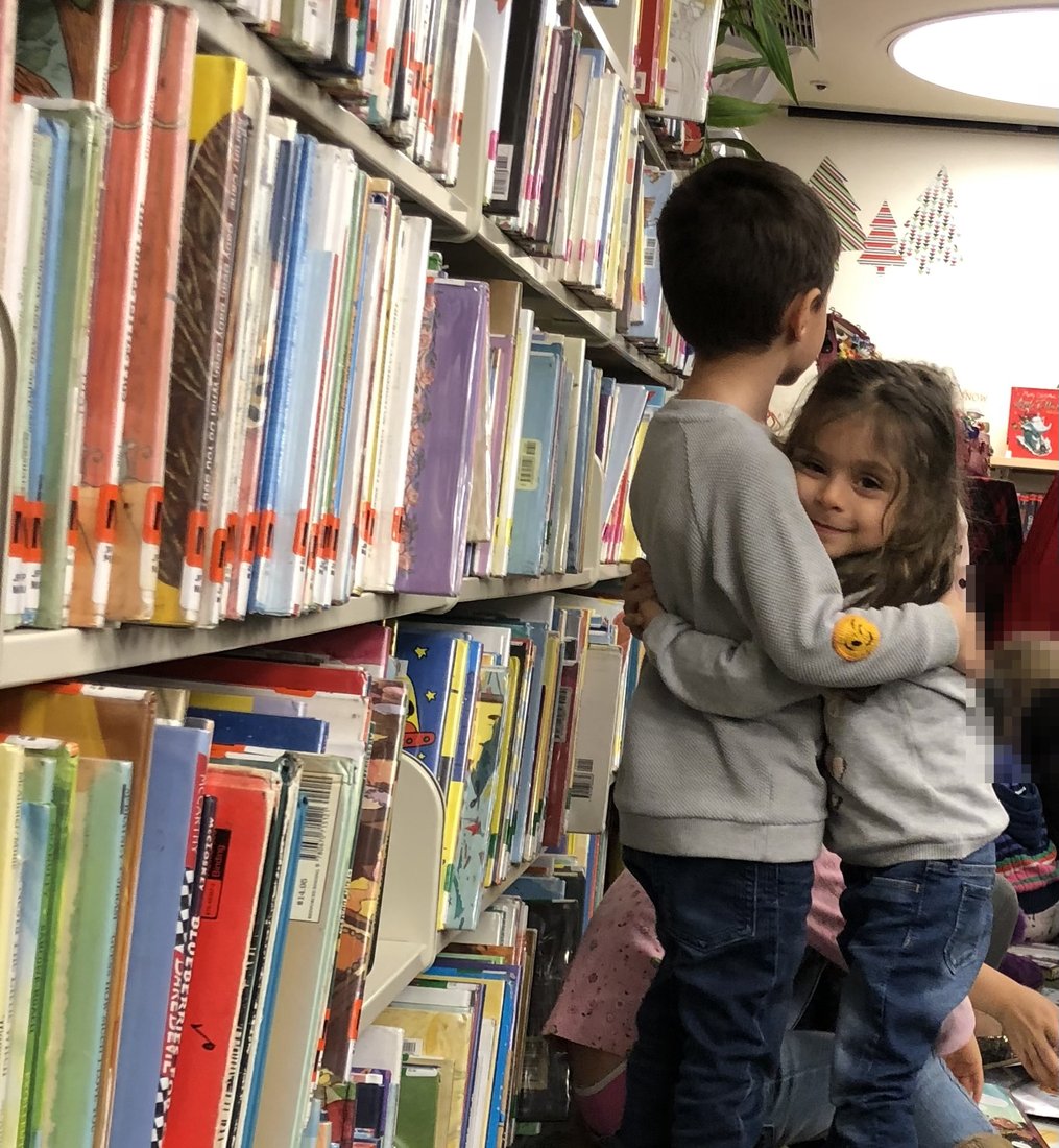 Aram and Alina hugging in the picture-book aisle at their local library